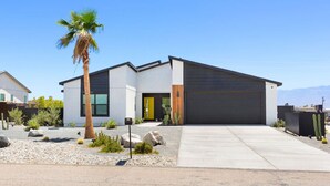 A modern two-story house with a garage, a palm tree, and desert landscaping.