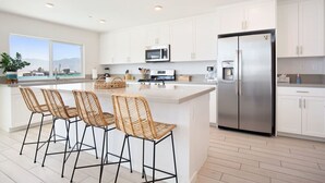 A modern kitchen with white cabinets, a stainless steel refrigerator, and a large island with bar stools.
