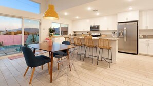 A modern kitchen with white cabinets, a stainless steel refrigerator, and a dining area with a wooden table and chairs.