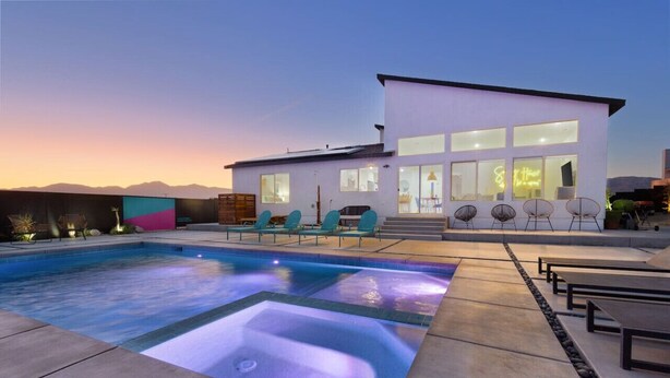 A modern house with a swimming pool, outdoor seating, and a well-lit entrance.