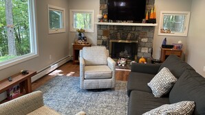 A living room with a fireplace, a sofa, a chair, and a television. - Berkshire Lake at the Pillow, and EV! (Otis)