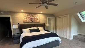 A bedroom with a bed, nightstands, a ceiling fan, a wall-mounted lamp, and a door. - Spacious Fly Creek Retreat – Game Rm, Creek Views & Minutes to Cooperstown & DP (Fly Creek)