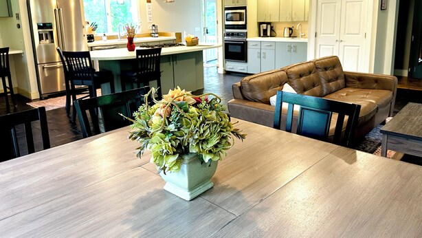 A modern kitchen with a dining area, a sofa, and a large potted plant. - Spacious Fly Creek Retreat – Game Rm, Creek Views & Minutes to Cooperstown & DP (Fly Creek)