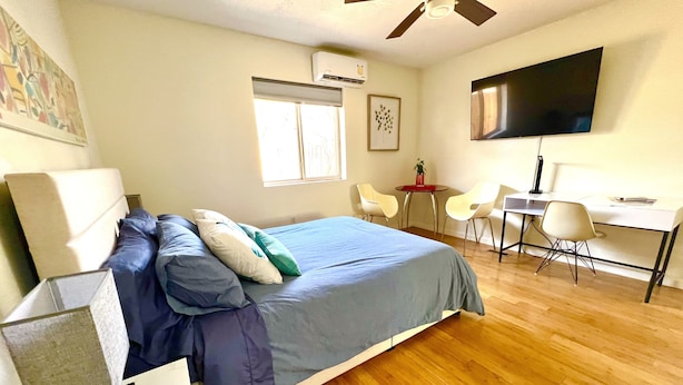 A bedroom with a bed, bedside table, desk, chairs, and a TV. - Garden Patio Studio near Bosque, Old Town (Albuquerque)