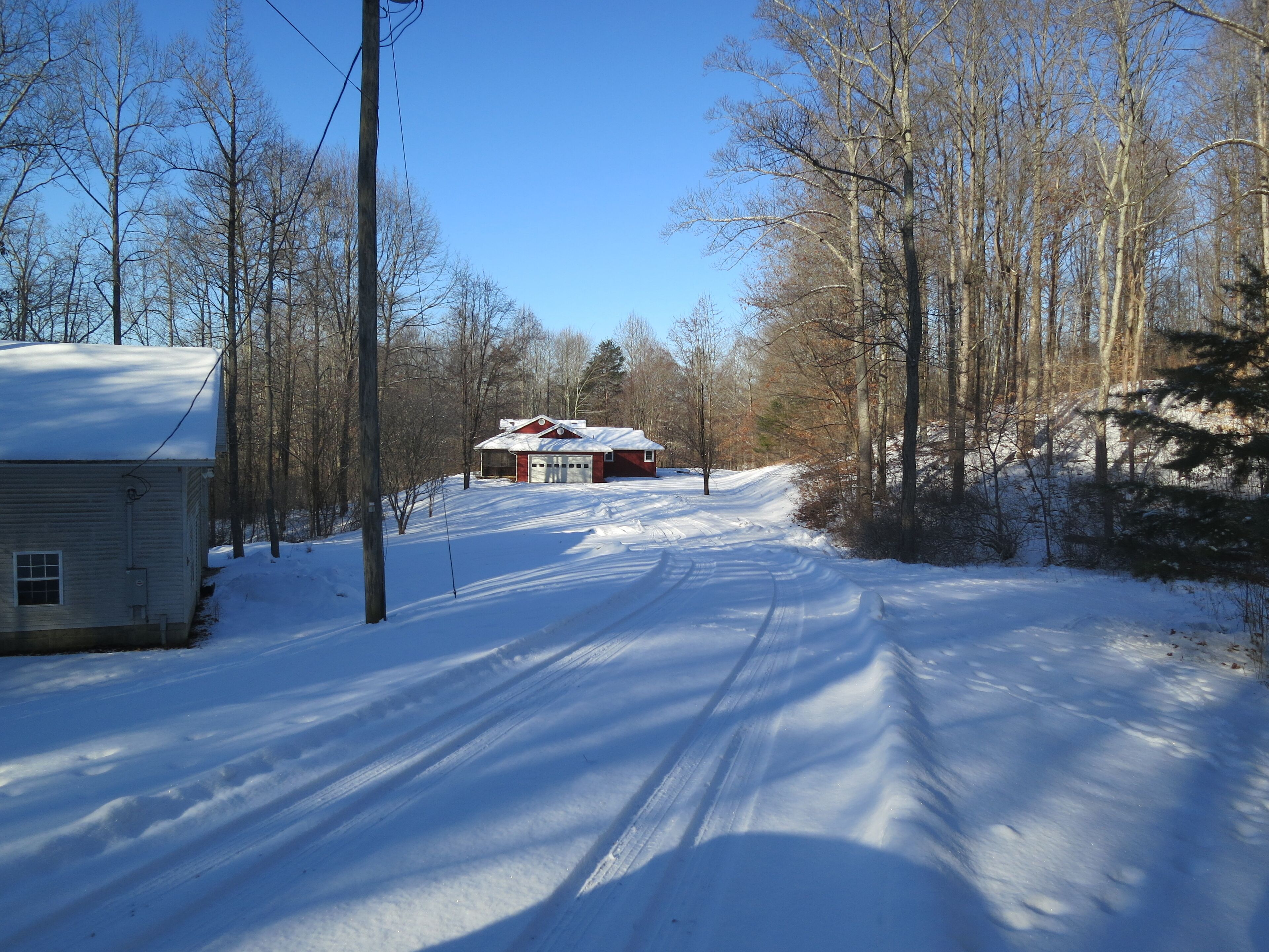 Een met sneeuw bedekte weg die naar een huis met een garage leidt.