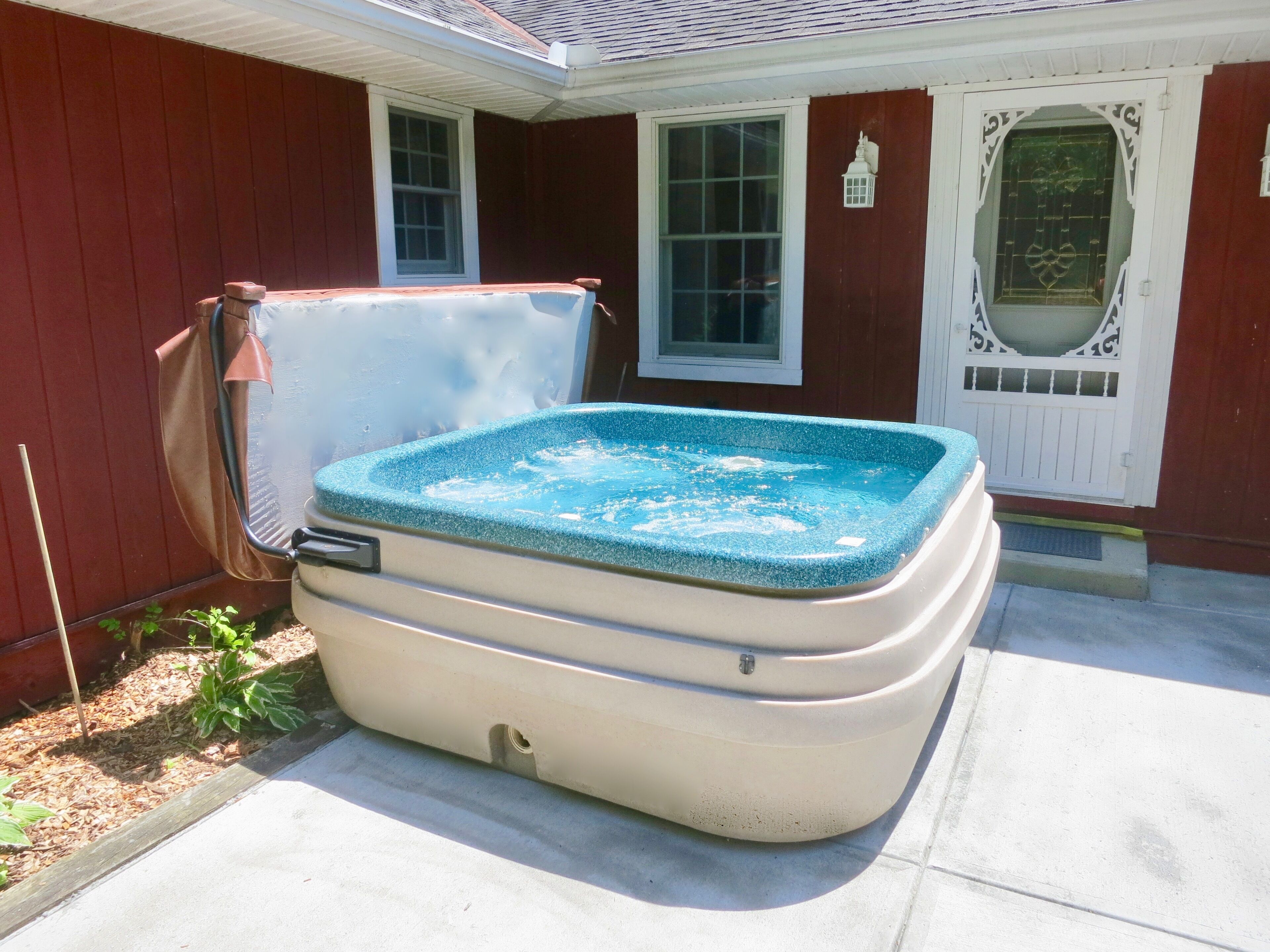 A hot tub in front of a house with a red exterior, a white door, and a window.
