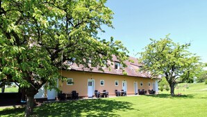 En tvåvåningsbyggnad med ett rött tegeltak och en beige fasad, omgiven av välskött gräsmatta och träd.