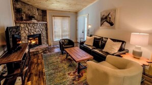 Una sala de estar acogedora con chimenea de piedra, mobiliario de cuero y un ventilador de techo.