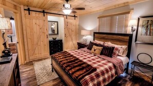 Un dormitorio con techo de madera, cama con ropa de cuadros, ventilador de techo y ventana con persianas.