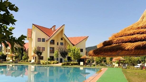 Un hôtel doté d’une piscine, d’une structure à toit de chaume et d’une pelouse bien entretenue.