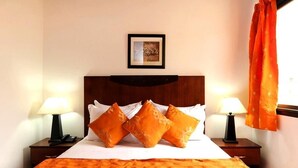 Une chambre d’hôtel avec un grand lit, deux lampes de chevet, une couvre-lit orange et un tableau encadré au mur.