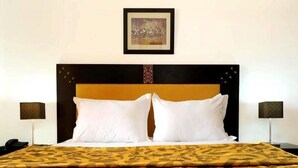 Habitación de hotel con una cama, dos lámparas de noche, una obra de arte enmarcada sobre la cama y una colcha estampada.