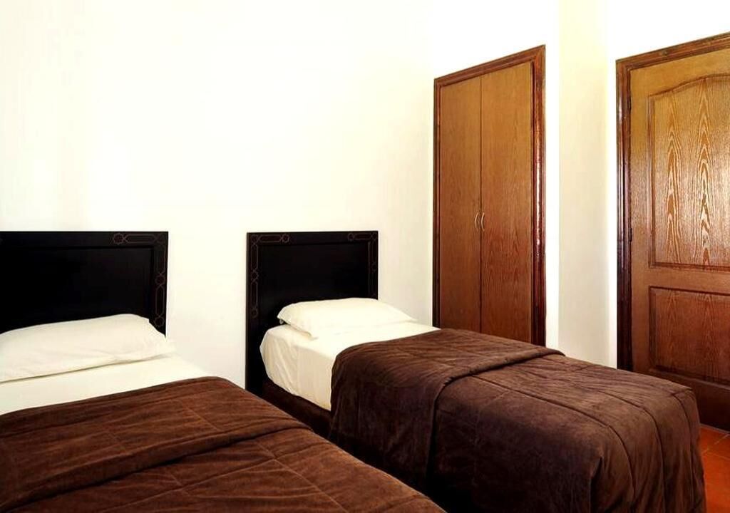 Une chambre d’hôtel avec deux lits, des armoires en bois et un mur blanc.