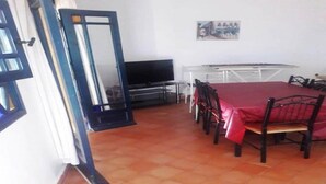 A dining area with a table and chairs, a television, and a white wall with a painting. - Residence Les Jardins de La Lagune 2275 (Oualidia)