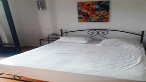 A bed with white linens, a metal headboard, and a colorful abstract painting on the wall. - Residence Les Jardins de La Lagune 2275 (Oualidia)