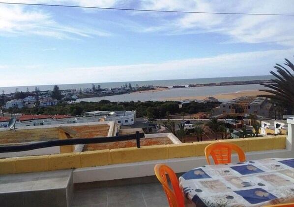 Eine Terrasse mit Tisch und Stühlen mit Blick auf eine Küstenlandschaft mit Gebäuden und Strand.