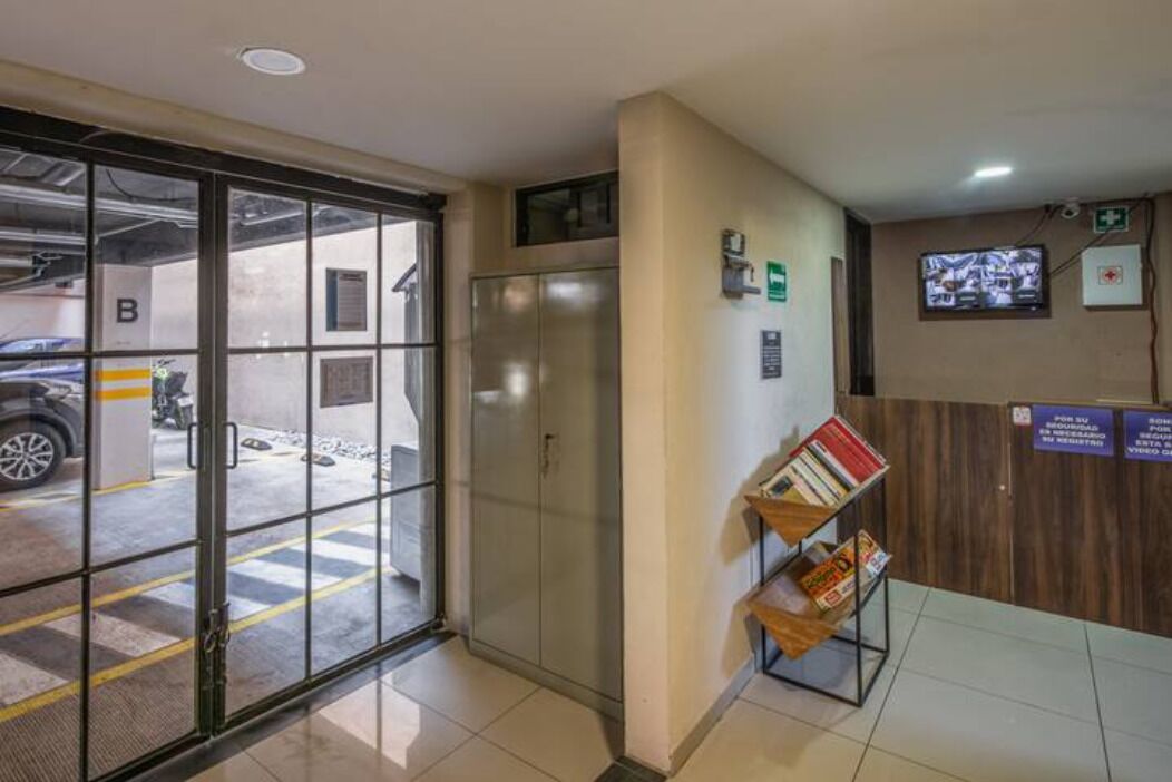 A reception area with a glass door entrance, a reception desk, a television screen, and a wall-mounted emergency exit sign.