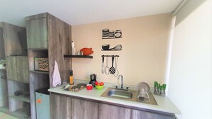 A compact kitchen with wooden cabinets, a sink, and a countertop with various kitchen items. - Suite Premium Increíble! A 2 Minutos DEL Tec! S06 (Ciudad López Mateos)