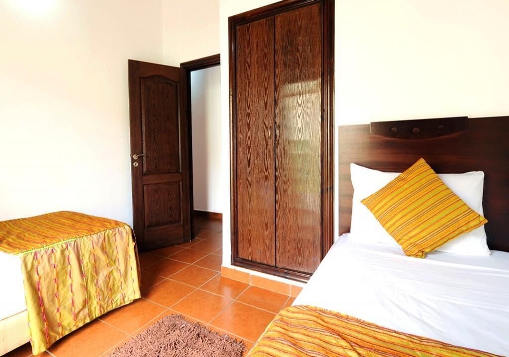 A hotel room with two single beds, a wooden wardrobe, a door, and a tiled floor.
