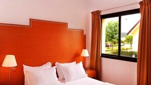 Een hotelkamer met een groot bed, twee bedlampen, een raam met gordijnen en uitzicht naar buiten.