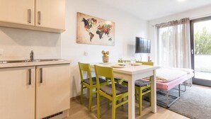 Una cocina moderna con armarios color beige, una mesa de comedor con sillas verdes, una obra de arte con un mapa mundial y un televisor.
