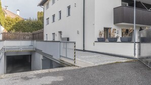 Un edificio moderno con entrada protegida por un portón, un pequeño espacio exterior con plantas en macetas y una escalera visible que conduce a un nivel superior.