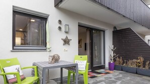 Un pequeño patio con dos sillas verdes, una mesa y una planta en maceta.