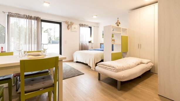 Habitación pequeña con cama, escritorio y silla. Cuenta con una ventana con cortinas, una estantería y un armario.