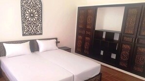 Un lit double avec du linge de lit blanc, une table de chevet et une armoire aux motifs complexes.