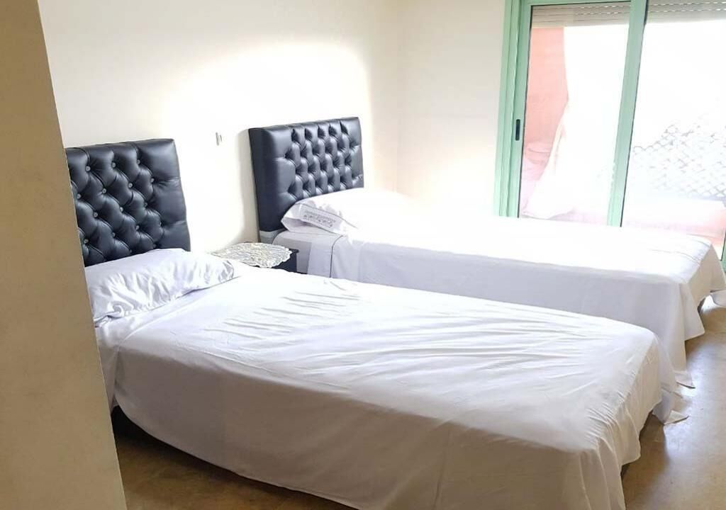 Habitació d'hotel amb dos llits, cadascun amb un capçal tapissat, roba de llit blanca i una petita taula de nit.