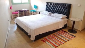 A bedroom with a large bed, a small round table, a chair, and a window with a green frame. - Superb apartment in Marrakech 4582 (Marrakech)