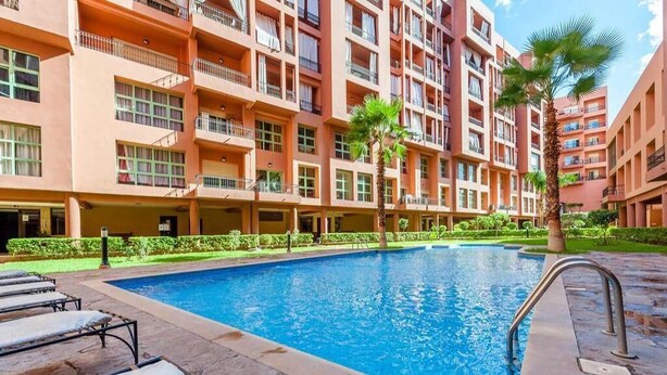 A swimming pool surrounded by a multi-story building with balconies. - Superb apartment in Marrakech 4582 (Marrakech)