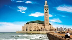 Eine große Moschee mit einem hohen Minarett am Meer, mit einem grünen Dach und aufwendigen Kacheln.