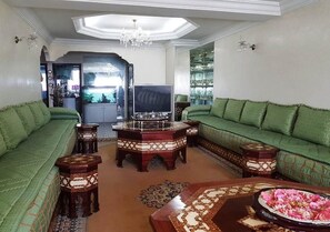 Un salon avec des canapés verts, un téléviseur et une table basse décorative.