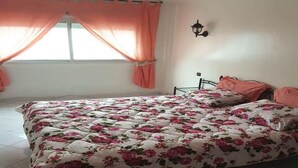Ein Schlafzimmer mit einem blumigen Bettüberwurf, einem Fenster mit Vorhängen und einer Wandleuchte.