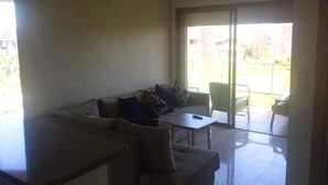 Un espacio de estar con un sofá, una mesita y un ventanal de vidrio que da a un balcón exterior.