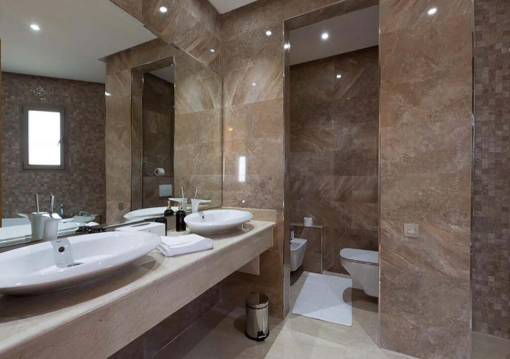 A modern bathroom with two sinks, a large mirror, and a toilet.