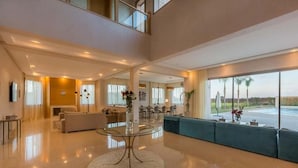 A spacious, modern living area with a high ceiling, a round glass coffee table, and a large window offering a view of palm trees. - Luxury villa in Marrakech 4613 (Marrakech)