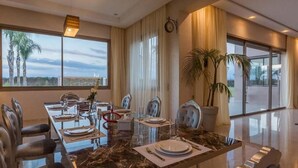A dining area with a marble table, modern chairs, and large windows offering a view of palm trees. - High standing villa in Marrakech 4614 (Marrakech)