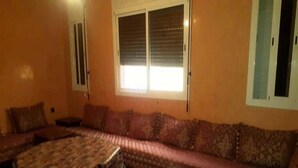 Una habitación con un sofá grande, una mesa pequeña y una ventana con persianas.