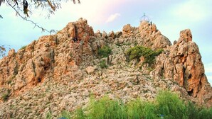 Una colina rocosa con un edificio pequeño en la cima, rodeada de árboles y farolas.