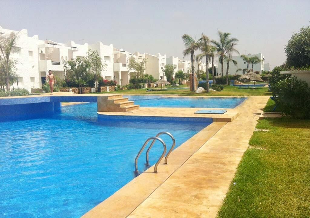 Une piscine à l’eau d’un bleu cristallin, entourée d’une promenade dallée et de palmiers.