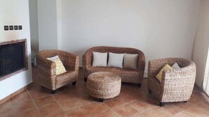 Ein Wohnzimmer mit Kamin, zwei Korbsessel, einer Couch und einem runden Hocker.