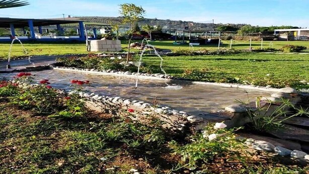 Ein angelegter Garten mit Wasserspiel, überdachter Sitzgelegenheit und Blick auf die Hügel im Hintergrund.