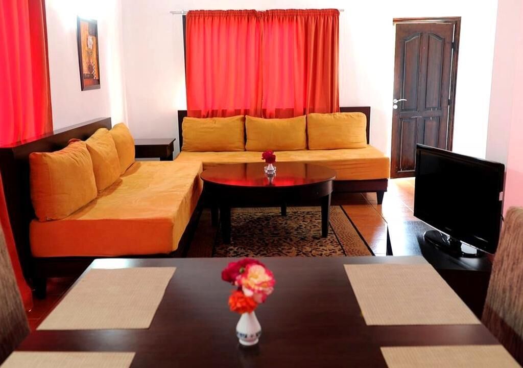 Una sala de estar con un sofá, una mesa de centro con un florero, un televisor y una puerta.