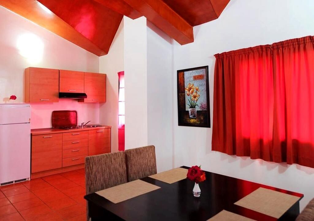 A compact kitchen with wooden cabinets, a dining table with chairs, and a red curtain.