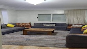Ein Wohnzimmer mit einem Ecksofa, einem Couchtisch und einem großen Fenster mit Jalousien.