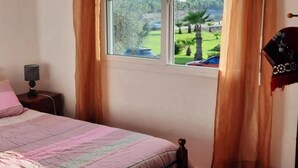 Ein Schlafzimmer mit einem Bett, einem Nachttisch, einer Lampe und einem Fenster mit Vorhängen.