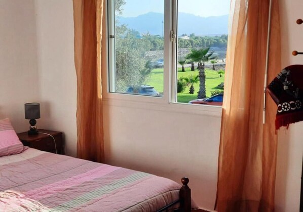 A bedroom with a bed, a nightstand, a lamp, and a window with curtains.