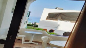 Blick vom Balkon mit einem weißen Tisch und Stühlen, einem kleinen Garten und einem Ausblick auf das Meer.
